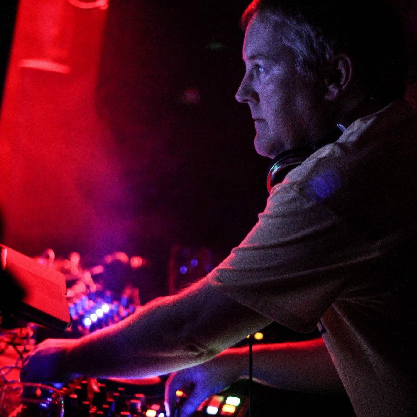 Nik Dee behind the decks, bathed in red and purple club light